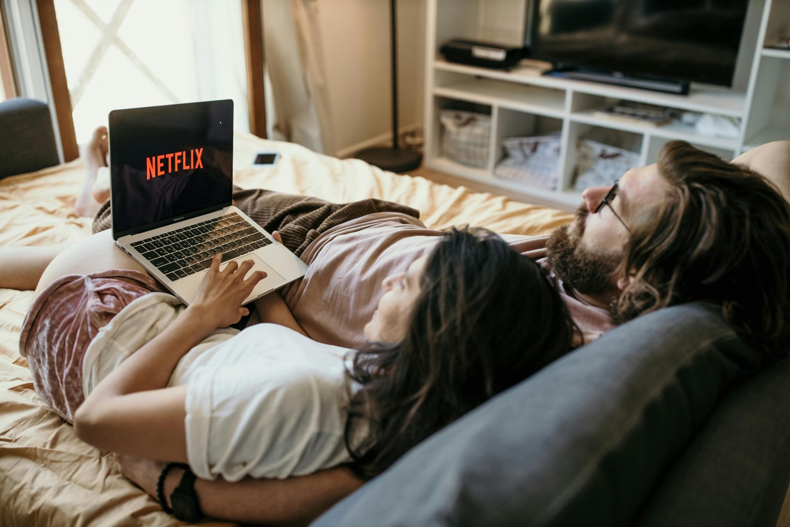A cozy couple lounging in bed, streaming Netflix together on a laptop, enjoying a peaceful moment with the vpn on for privacy and protection